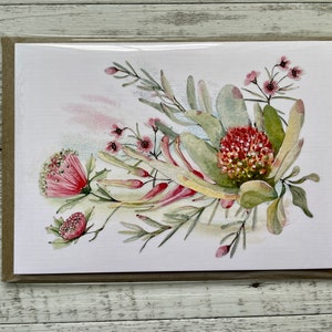 Op de afbeelding: Een aquarel schilderij van een boeket roze en rode bloemen met groene bladeren. De bloemen zijn in een losse, natuurlijke stijl gerangschikt. De achtergrond is een zachte, aquarel was van roze en blauw.