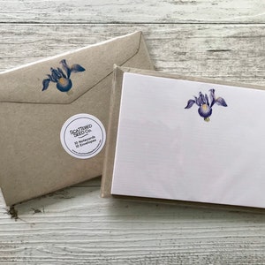May include: A set of 10 blank note cards with envelopes featuring a purple iris flower illustration. The cards are packaged in a brown envelope with a white sticker that says "Scattered Seed Co. 10 Notecards 10 Envelopes".