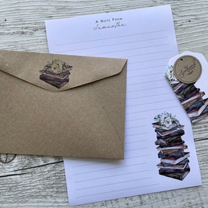 May include: A brown envelope with a sticker of a stack of books with white flowers on top. A white sheet of paper with lines and a sticker of a stack of books with white flowers on top. A white tag with the text "Sentimental  Edition" in a circle and the text "For you" below the circle.