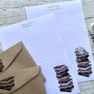 May include: Two white lined stationery note cards with the text "A Note From Joshua" and "A Note From Samantha" printed on them. Each card features a stack of books with a floral design on top. The cards are accompanied by two brown envelopes with a stack of books design on the front.