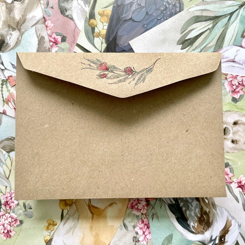 May include: A brown paper envelope with a floral design on the flap. The design features red flowers and green leaves. The envelope is rectangular and appears to be made of recycled paper.