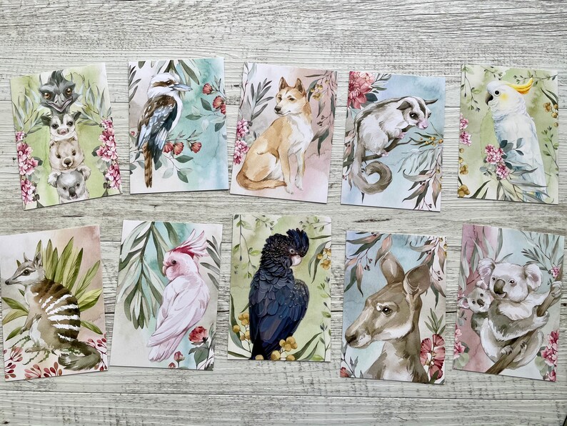 May include: A collection of ten watercolor art prints featuring Australian animals. Each print showcases a different animal, including a kookaburra, dingo, and koala, set against a backdrop of foliage and flowers. The prints have a soft, pastel color palette.