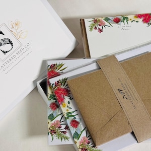 May include: A set of floral stationery in a white box. The stationery features a floral design with pink, white, and green flowers. The box is labelled "Scattered Seed Co. Quality Stationery".
