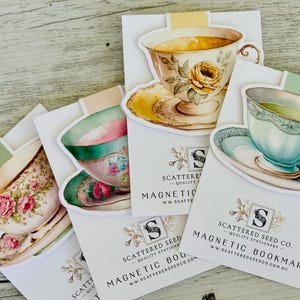 May include: Four magnetic bookmarks shaped like teacups with floral designs. Each bookmark has a white background with the text "SCATTERED SEED CO. QUALITY STATIONERY MAGNETIC BOOKMARK ww.SCATTEREDSEEDCO.COM.AU" printed on it.