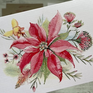 Op de afbeelding: Een aquarel schilderij van een kerstster bloem met roze en rode bloemblaadjes, omringd door groene bladeren en andere kleine bloemen. De achtergrond is licht beige.