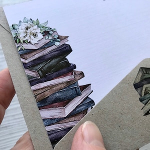 Puede incluir: Una pila de libros antiguos con un arreglo floral en la parte superior. Los libros son de varios tonos de marr&oacute;n, azul y morado. El arreglo floral es blanco y verde.