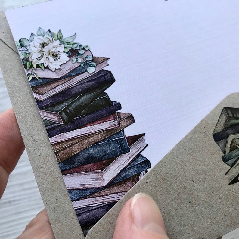 Puede incluir: Una pila de libros antiguos con un arreglo floral en la parte superior. Los libros son de varios tonos de marr&oacute;n, azul y morado. El arreglo floral es blanco y verde.