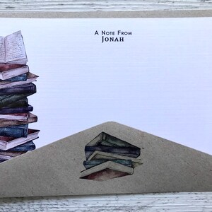 Puede incluir: Una tarjeta blanca con una solapa de sobre marr&oacute;n. La tarjeta tiene una pila de libros en el lado izquierdo y el texto "A Note From Jonah" en la parte superior. La solapa del sobre tiene una pila de libros en la parte inferior.