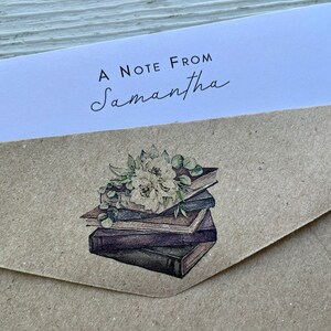 May include: A brown paper envelope with a white label that says "A Note From Samantha". The envelope has a sticker with a watercolor illustration of a stack of books with flowers on top.