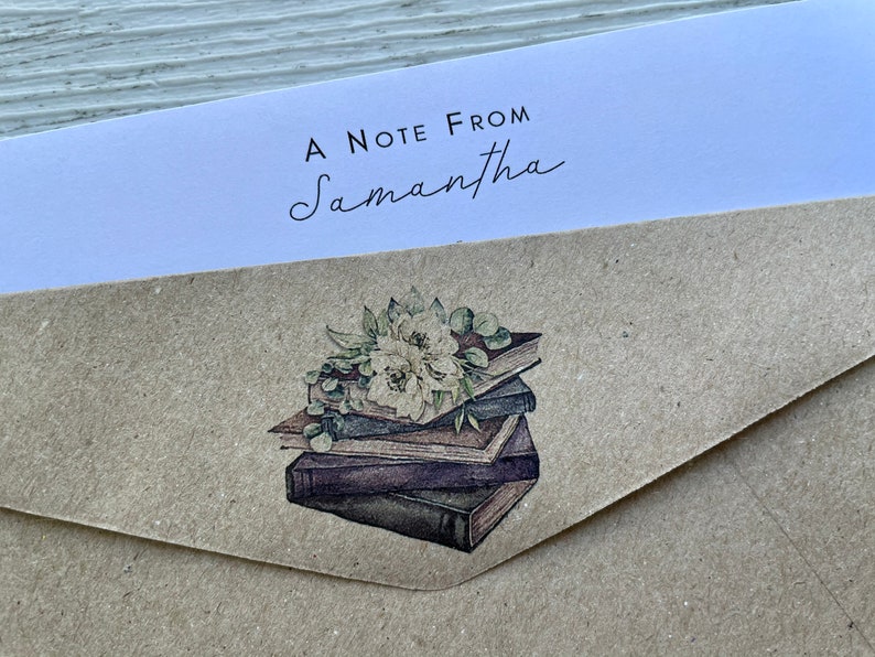 May include: A brown paper envelope with a white label that says "A Note From Samantha". The envelope has a sticker with a watercolor illustration of a stack of books with flowers on top.