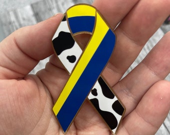 May include: A yellow, blue, and black ribbon with a cow print design. The ribbon is tied in a bow.