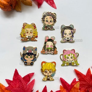 Könnte beinhalten: Set mit 7 goldfarbenen Emaille-Pins mit Charakteren aus dem Anime Demon Slayer. Die Pins sind bunt und zeigen verschiedene Charaktere mit unterschiedlichen Gesichtsausdrücken.