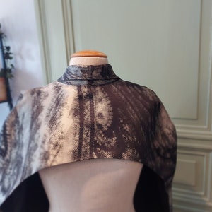 May include: A black and white patterned cape with a high neck. The cape is made of a soft, textured fabric.