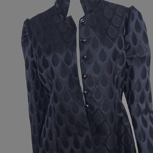 May include: A black jacket with a stand-up collar and a button-up front. The jacket has a pattern of small teardrop shapes all over it. The text "IMAGINEZ - VOUS dedans ???" is written on the jacket.