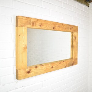 May include: A rectangular mirror with a thick, natural wood frame. The frame is made of unfinished, light brown wood with a knotty grain pattern.