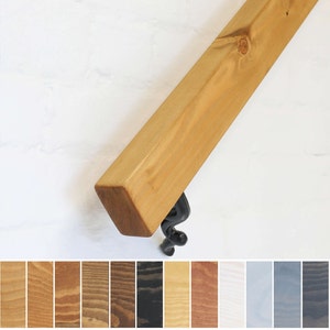 May include: A wooden handrail with a natural finish and a black metal bracket. The handrail is shown against a white background. A variety of wood stain colours are shown below the handrail.