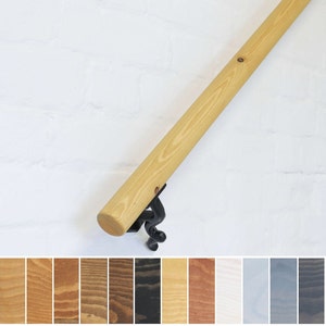May include: A wooden handrail with a natural finish and a black metal bracket. The handrail is shown against a white brick wall. The image also includes a selection of wood stain colours.