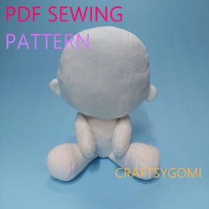 May include: A white plush doll with a round head, small ears, and seated pose. The doll is made of soft material and has a simple design. Text on the image reads "PDF SEWING PATTERN" and "CRAFTSYGOMI". The background is a solid light blue.