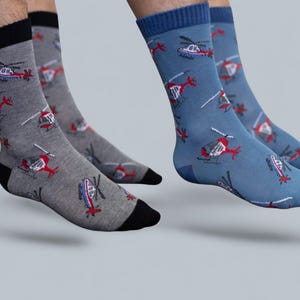 Puede incluir: Dos pares de calcetines deportivos, uno gris y otro azul, cada uno con un estampado de helicópteros rojos y blancos. Los calcetines grises tienen talones y dedos negros, mientras que los calcetines azules tienen talones y dedos azules.
