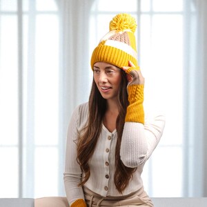 Peut inclure: Un bonnet en tricot jaune, blanc et beige avec un pompon assorti et des mitaines. Le bonnet et les gants ont un motif en tricot torsadé. La femme sur l'image porte une chemise boutonnée crème.