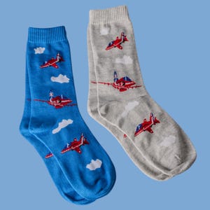 Puede incluir: Un par de calcetines con un diseño de avión rojo, blanco y azul. Un calcetín es azul y el otro es gris.