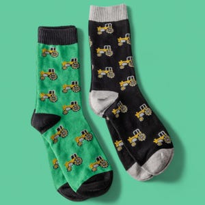 Può includere: Un paio di calzini con stampa di trattore. Un calzino è verde con bordini neri e l'altro è nero con bordini grigi.