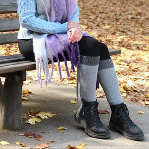 Puede incluir: Una persona sentada en un banco de madera lleva un suéter azul claro, una bufanda morada y blanca con flecos, leggings negros, calentadores grises y botas negras con cordones. El fondo presenta hojas caídas.
