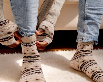 Puede incluir: Una persona se pone calcetines beiges con un estampado geométrico de líneas y formas marrones y rojas. Los calcetines se combinan con vaqueros azul claro y guantes sin dedos beiges.