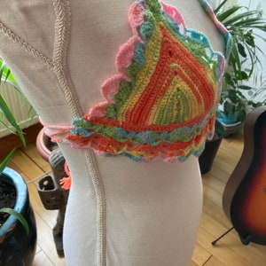 May include: A colorful crocheted halter top with a rainbow striped pattern. The top is made with a variety of colors, including pink, orange, yellow, green, and blue.