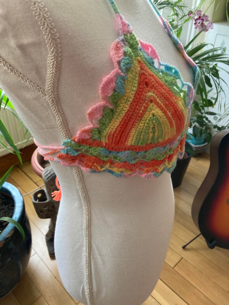 May include: A colorful crocheted halter top with a rainbow striped pattern. The top is made with a variety of colors, including pink, orange, yellow, green, and blue.