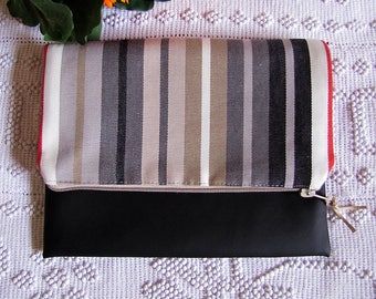May include: A black and striped clutch with a fold-over flap. The flap features vertical stripes in shades of gray, beige, and white. The clutch has a red trim and a zipper closure with a tan pull. The bottom half of the clutch is solid black.