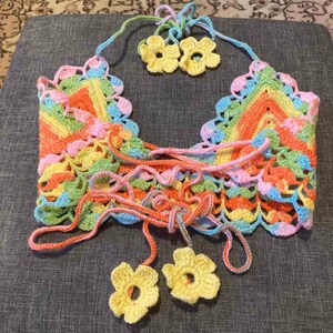 May include: A colorful crocheted top with a rainbow striped pattern and yellow flower accents. The top has a lace-up front and is made with a delicate crochet stitch.
