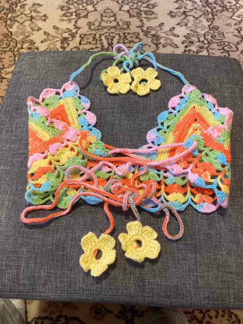 May include: A colorful crocheted top with a rainbow striped pattern and yellow flower accents. The top has a lace-up front and is made with a delicate crochet stitch.