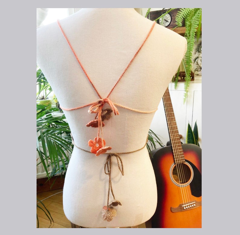 May include: A crocheted halter top with a brown and orange ombre color scheme. The top features a tie closure at the back and has crocheted flower accents.