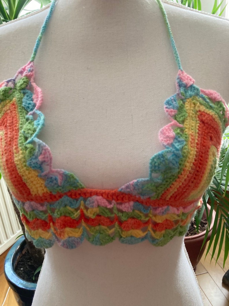May include: A rainbow crochet halter top with a scalloped edge. The top is made with a variety of colors, including pink, blue, green, yellow, and orange.