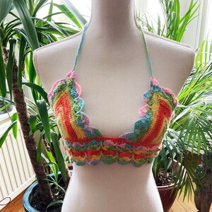 May include: A rainbow crochet top with a scalloped edge. The top is made with a variety of colors, including pink, orange, yellow, green, and blue.