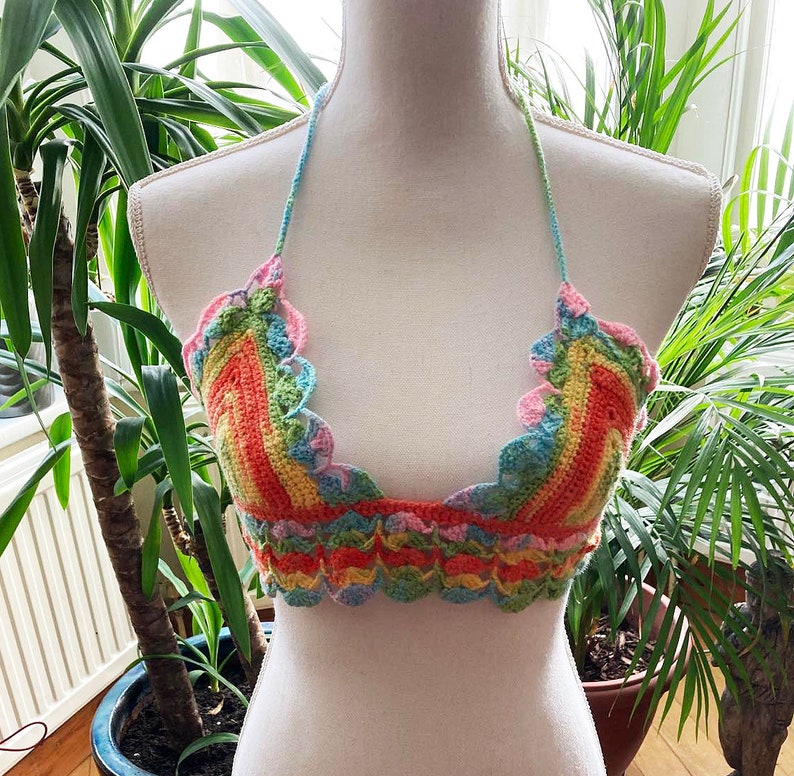 May include: A rainbow crochet top with a scalloped edge. The top is made with a variety of colors, including pink, orange, yellow, green, and blue.