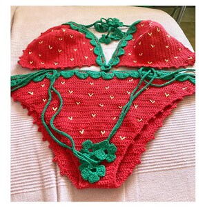 May include: Red and green crochet bikini top and bottom with a strawberry design. The bikini is handmade and has a scalloped edge.