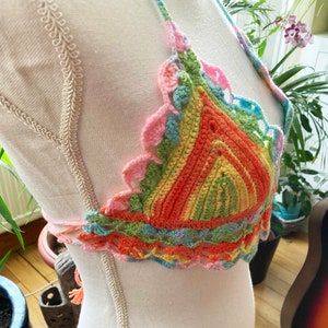 May include: A colorful crocheted halter top with a rainbow striped pattern and scalloped edges.