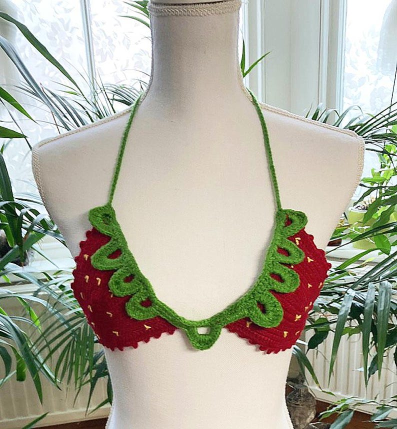 May include: A red and green crocheted bikini top shaped like a strawberry. The top has a green crocheted leaf design and a red crocheted strawberry design.
