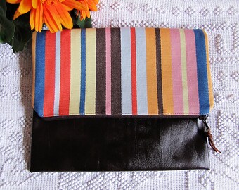 May include: A striped fabric clutch with a brown leather flap and zipper closure. The fabric is a mix of red, orange, yellow, blue, and white stripes.