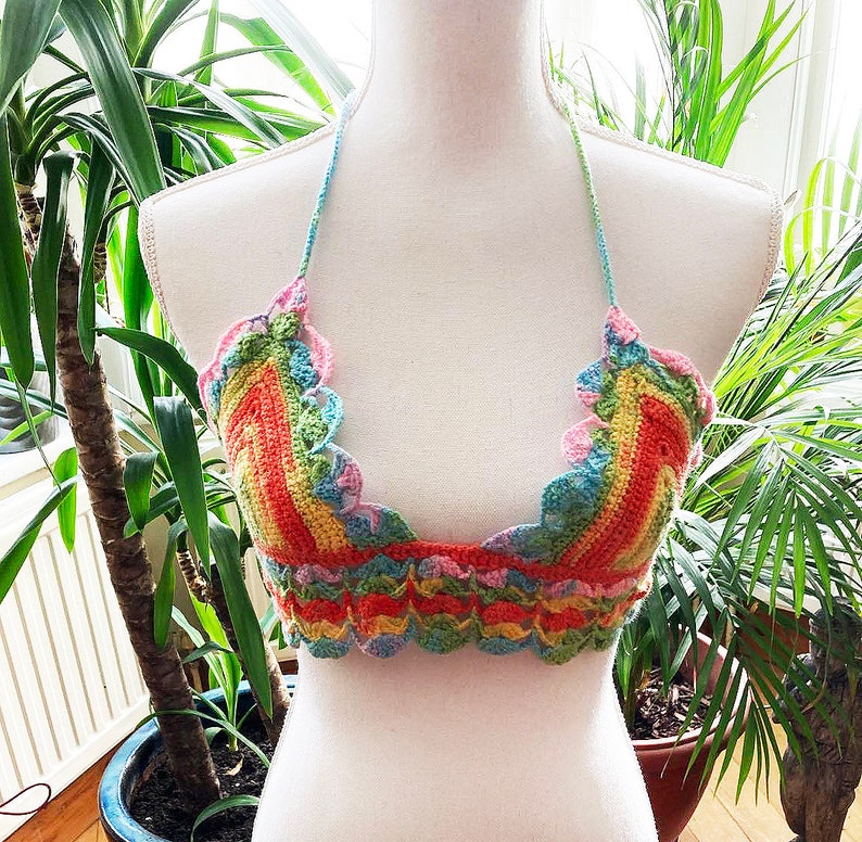 May include: A rainbow crochet top with a scalloped edge. The top is made with a variety of colors, including pink, orange, yellow, green, and blue.