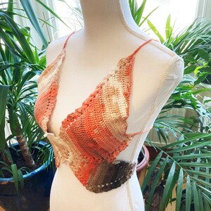 May include: A crocheted top with a multi-colored ombre design in shades of brown, orange, and white. The top has a halter style with a V-neck and a tie closure at the back.