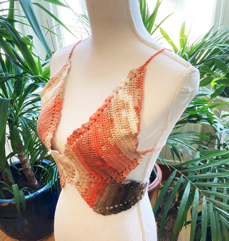 May include: A crocheted top with a multi-colored ombre design in shades of brown, orange, and white. The top has a halter style with a V-neck and a tie closure at the back.
