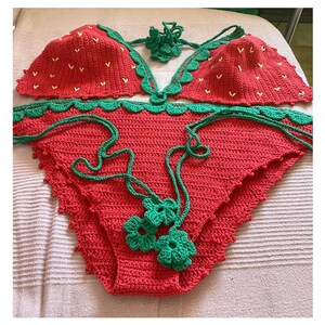 May include: A red and green crocheted bikini with a strawberry pattern. The bikini top has a halter style and the bottom is a high-waisted style.