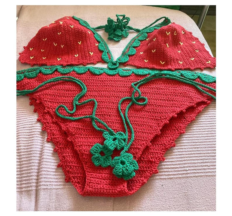May include: A red and green crocheted bikini with a strawberry pattern. The bikini top has a halter style and the bottom is a high-waisted style.