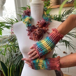 May include: A colourful crochet necklace and matching fingerless gloves are displayed on a mannequin. The handmade set features a vibrant mix of colours, including red, yellow, green, and blue. The gloves have a ruffled edge.