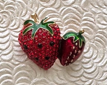 May include: A pair of strawberry-shaped brooches. One brooch is a large, red strawberry encrusted with red rhinestones and black accents. The other is a smaller, red enameled strawberry with green leaves and gold accents.