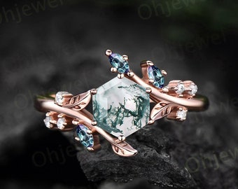 Op de afbeelding: Een roségouden ring met een zeshoekige mosagaat middensteen. De ring is versierd met blad- en wingerddetails, en kleine, ronde en marquise-geslepen edelstenen. Het ontwerp van de ring heeft een natuurlijk, botanisch thema.