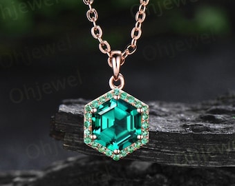 May include: A rose gold necklace with a hexagonal pendant featuring a large emerald green gemstone surrounded by smaller emerald green gemstones.